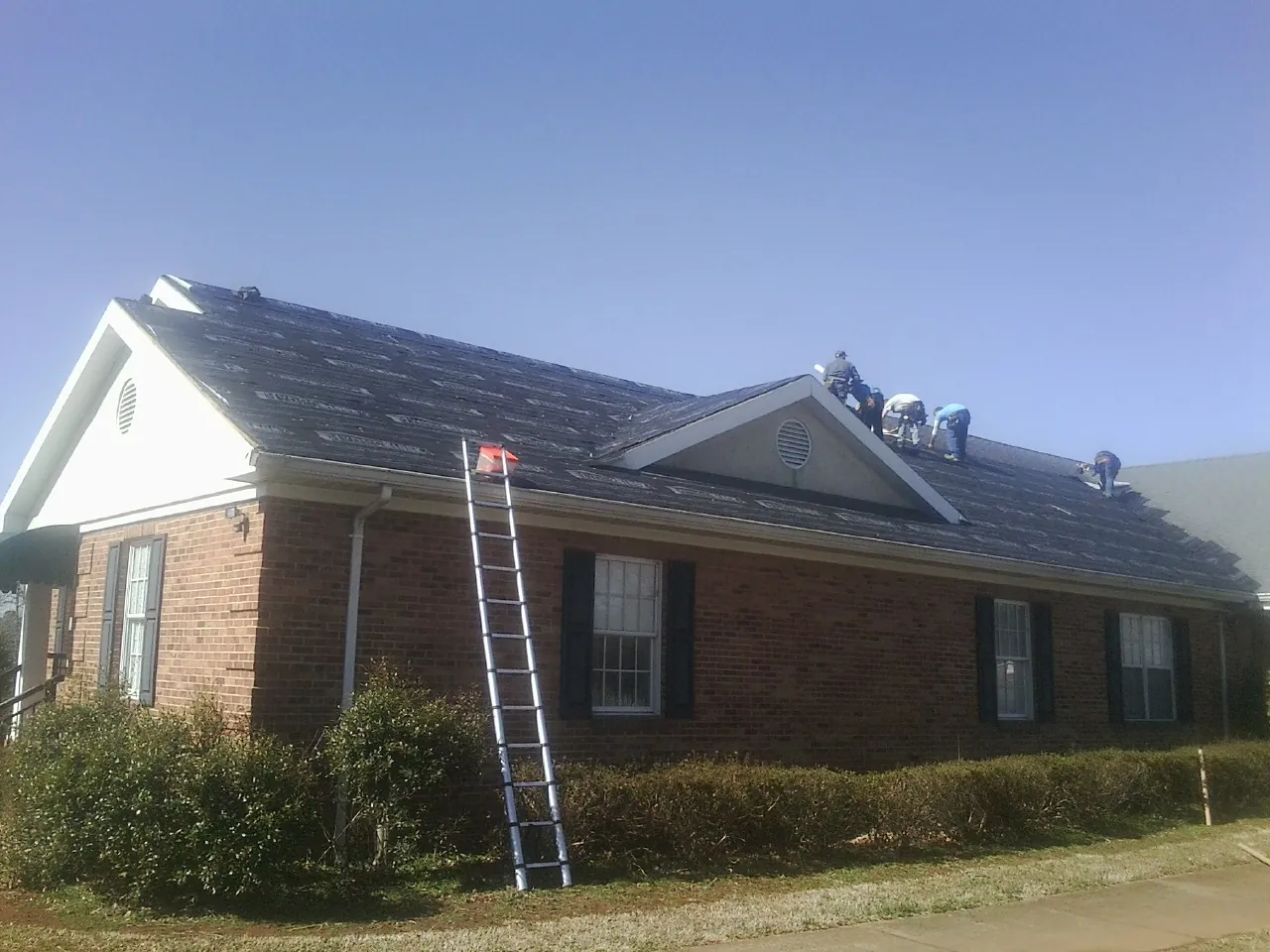 Crew tearing shingles off a brick ranch roof with a ladder set — Emergency Roof Repair work by our crew in Kenosha
