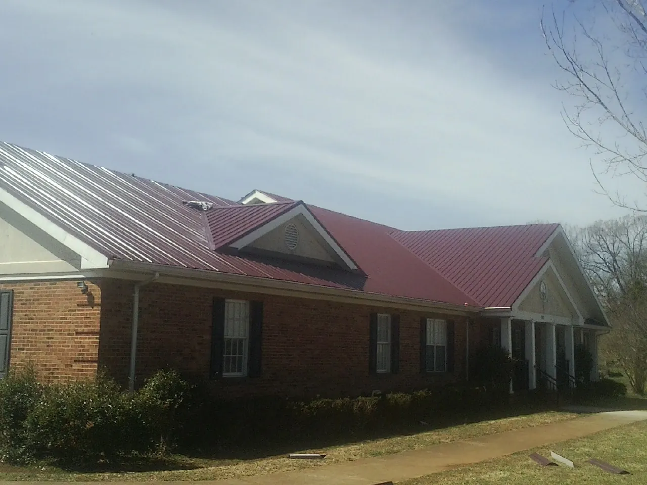 Red metal roof with gabled entries on a long brick building, from a Hail Damage Roof Repair job in Kenosha