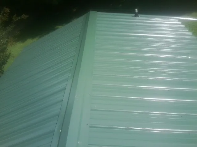 New green metal panels meeting at the ridge of a roof — Flat Roof Repair work by our crew in Kenosha