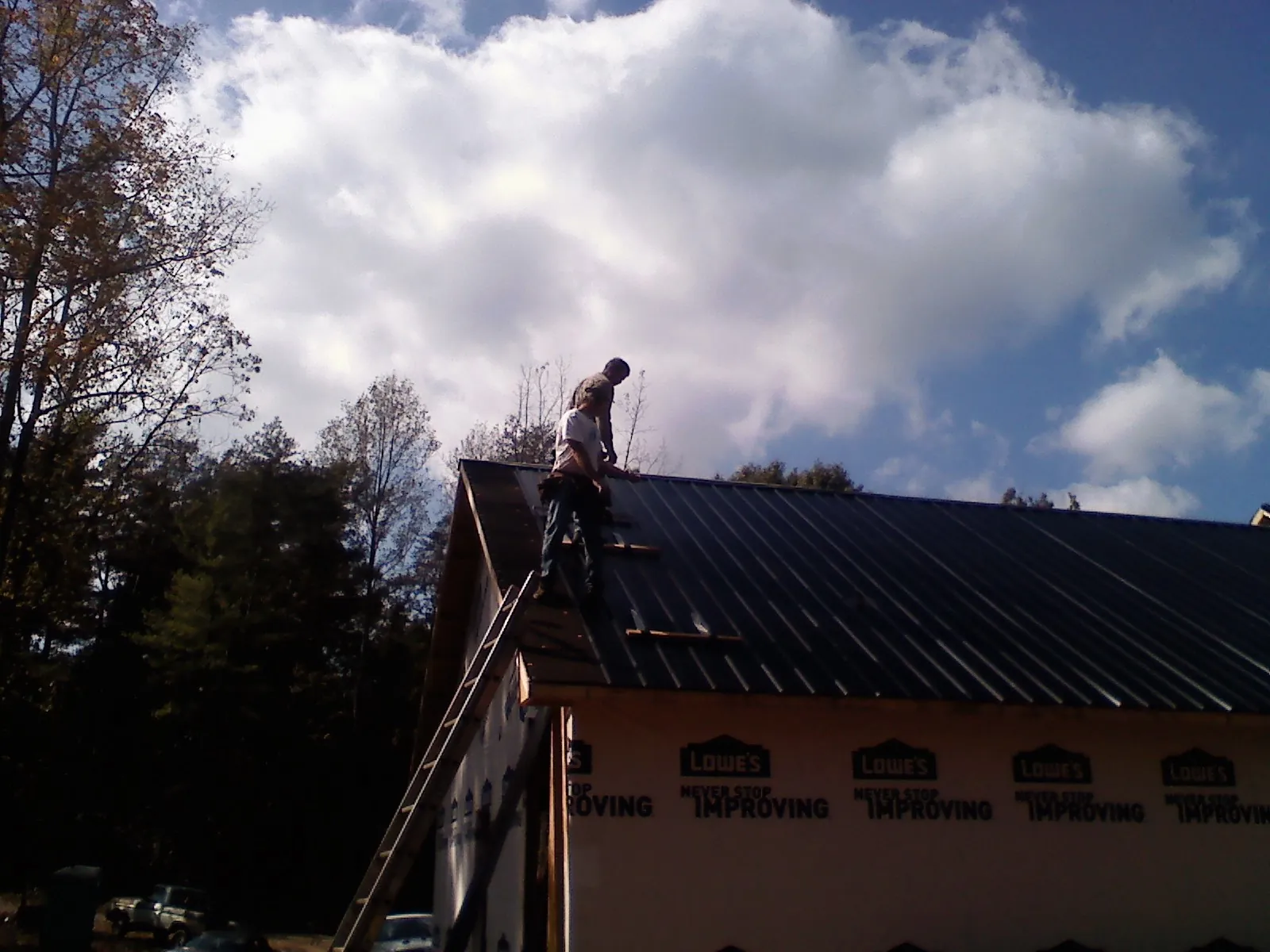 Roofer fastening dark metal panels high against a cloudy sky, from a Roof Inspection job in Kenosha