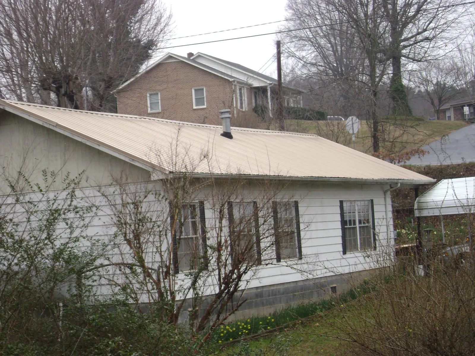 Tan metal roof on a white sided house set into a hillside — Commercial Roofing by Roofing Brothers in Kenosha